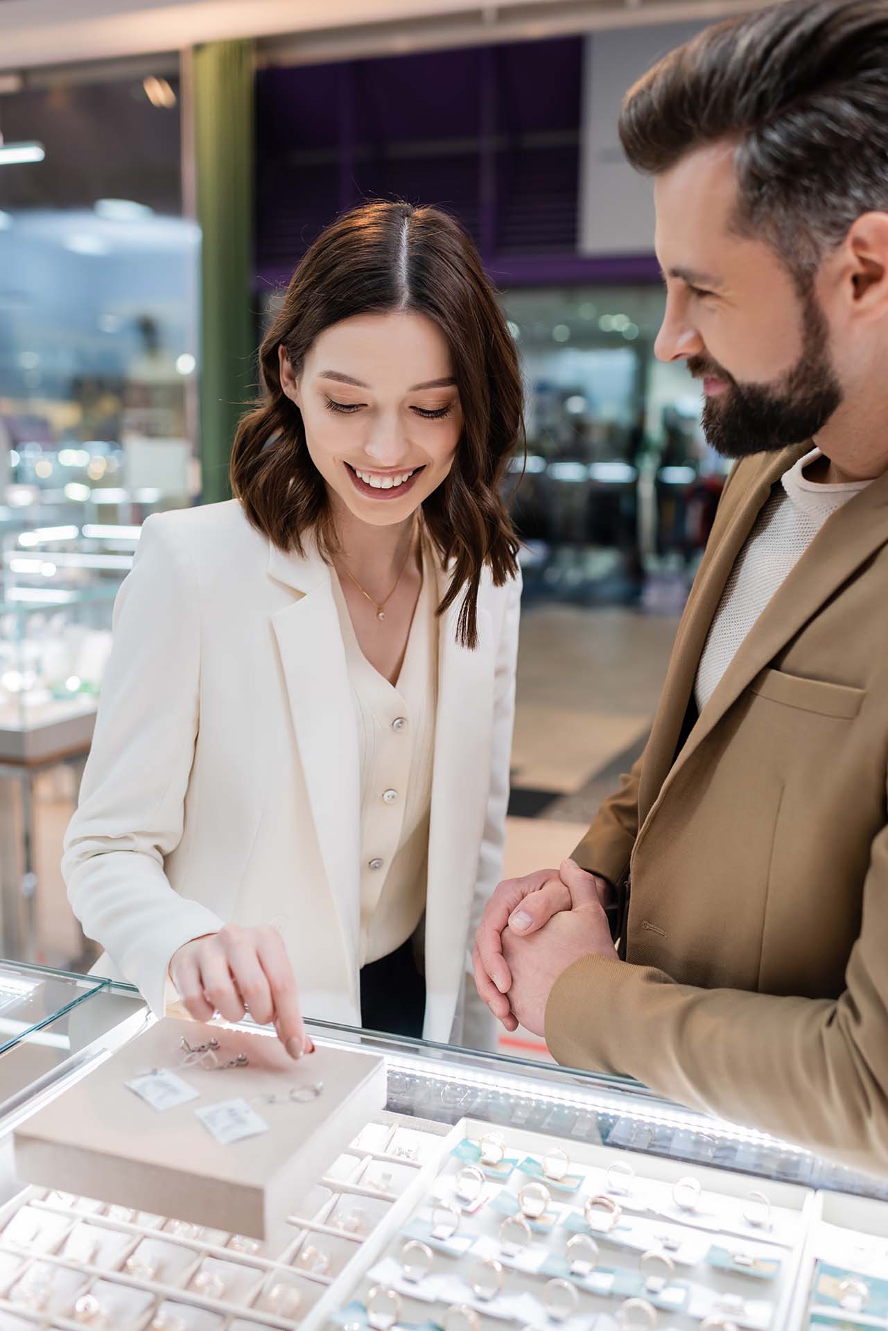 Smiling woman choosing rings near blurred boyfriend in jewelry store.